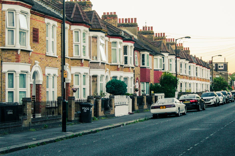 A row of Victorian-style terraced houses on Dartmouth Park Road with white-painted facades, decorative cornices, and black wrought-iron balconies. The street features parked cars including a silver st